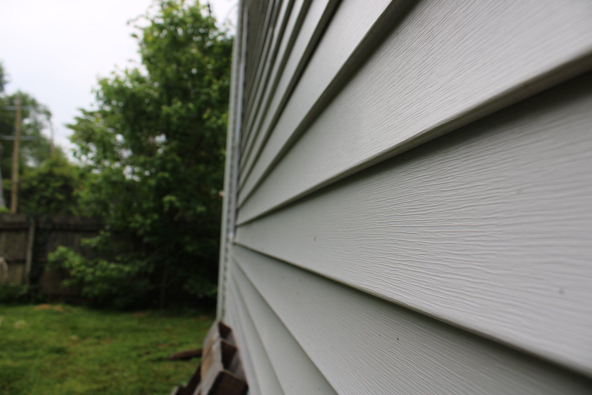 A close up of a white siding on a house with trees in the background.