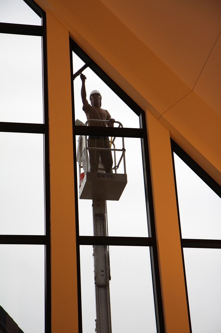 Person in lift cleaning large, geometric windows of a building.