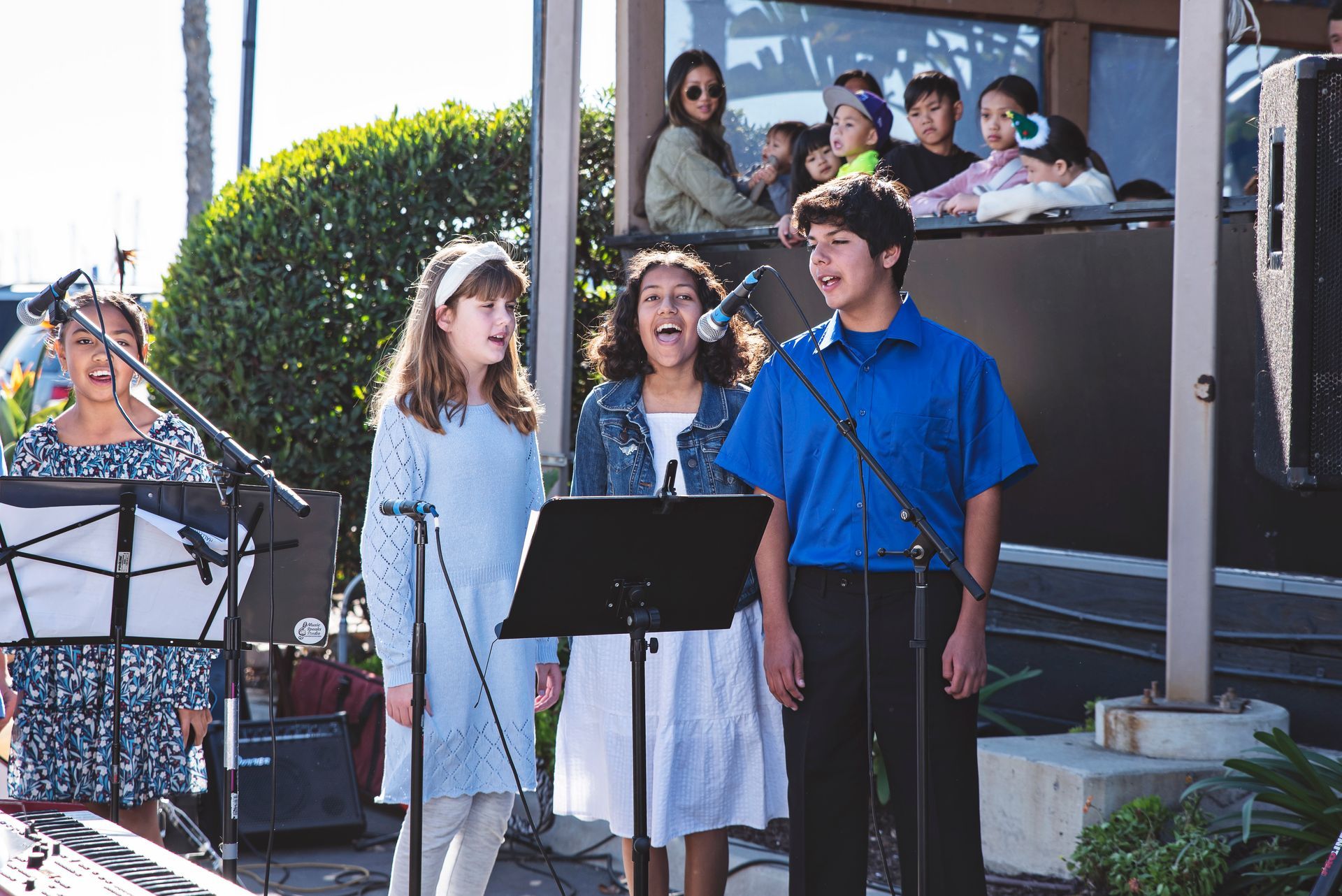 A group of children are singing into microphones in front of a crowd.