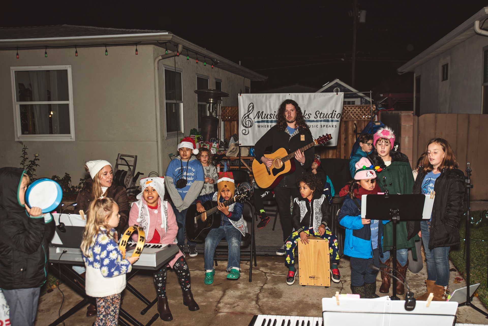 A group of children are standing around a man playing a guitar.
