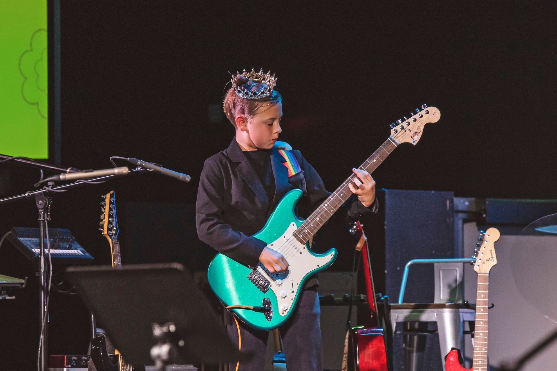 A young boy is playing a green electric guitar on a stage.