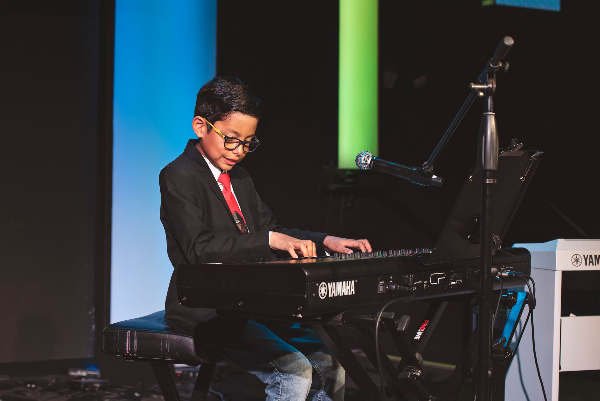 A young boy is playing a keyboard on a stage.