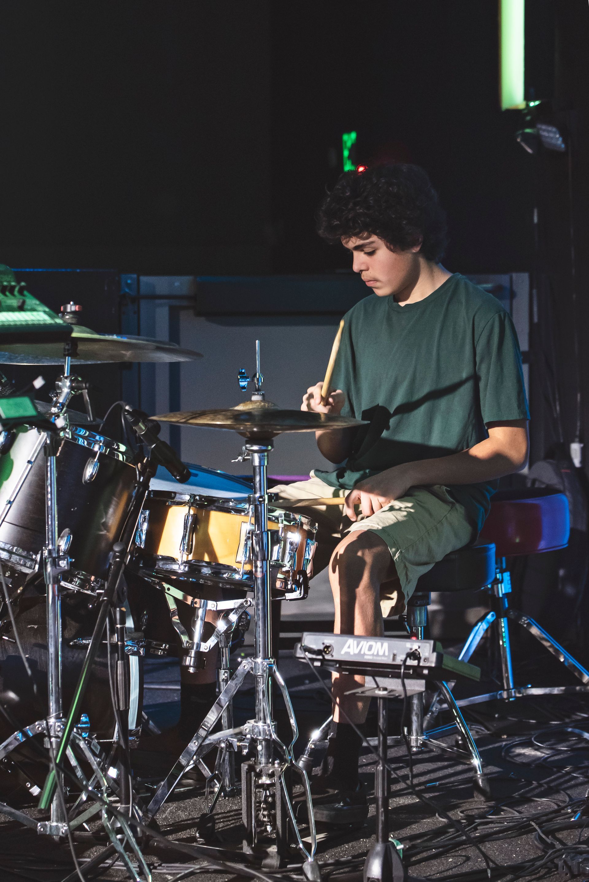A man in a green shirt is playing drums on a stage.