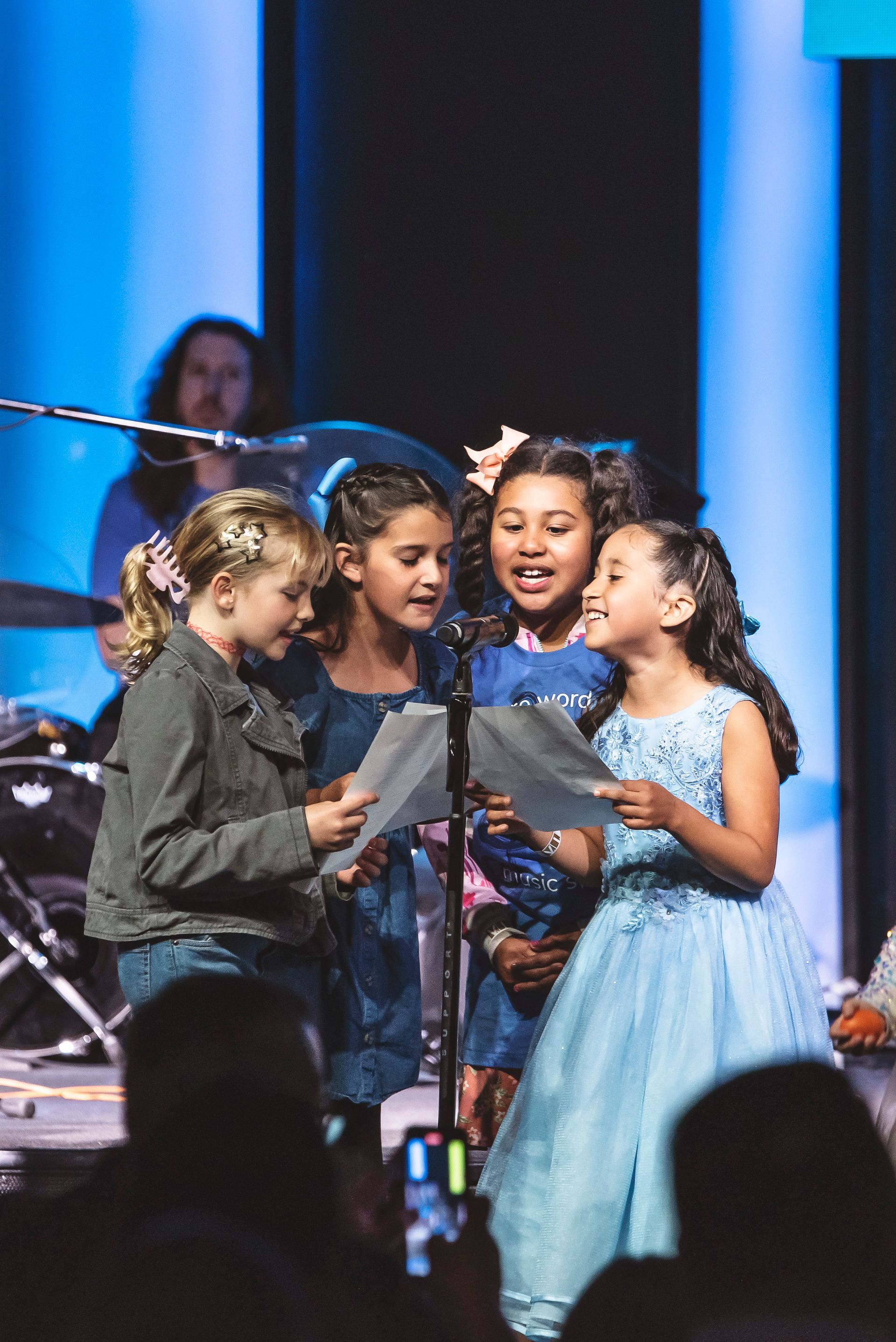 A group of young girls are singing into microphones on a stage.