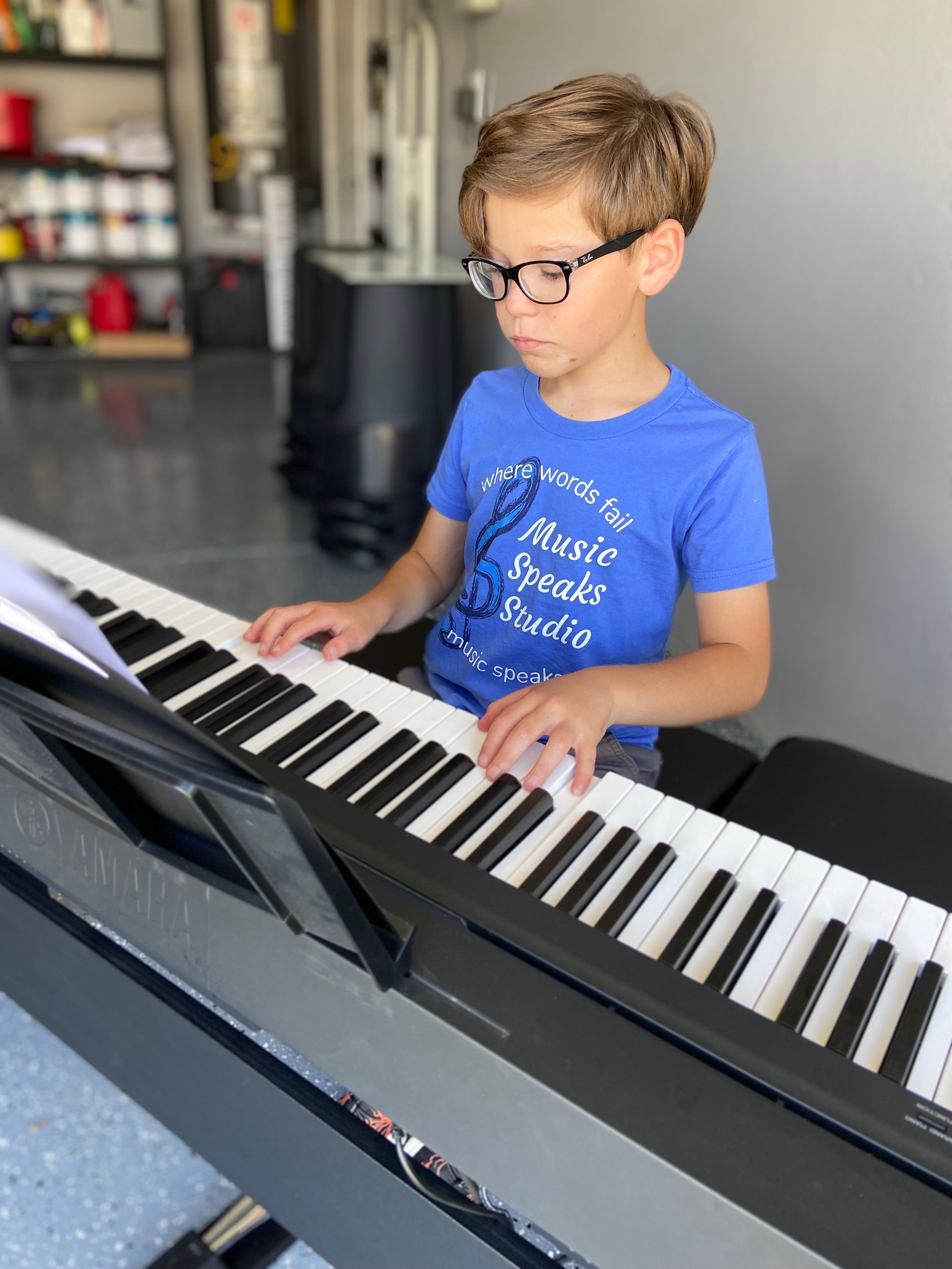 A young boy is playing a piano in a garage.