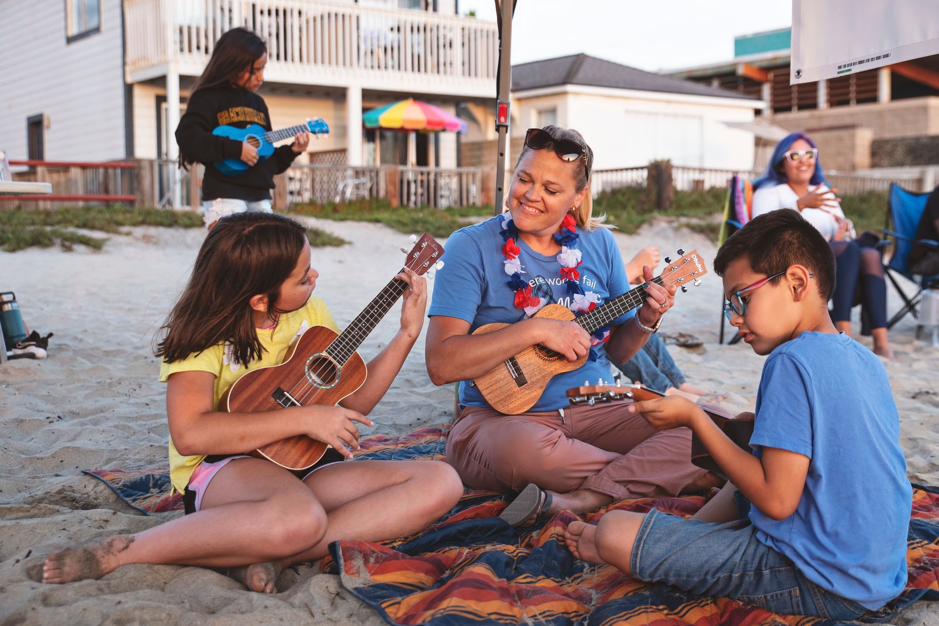 A group of people are sitting on the beach playing ukuleles.