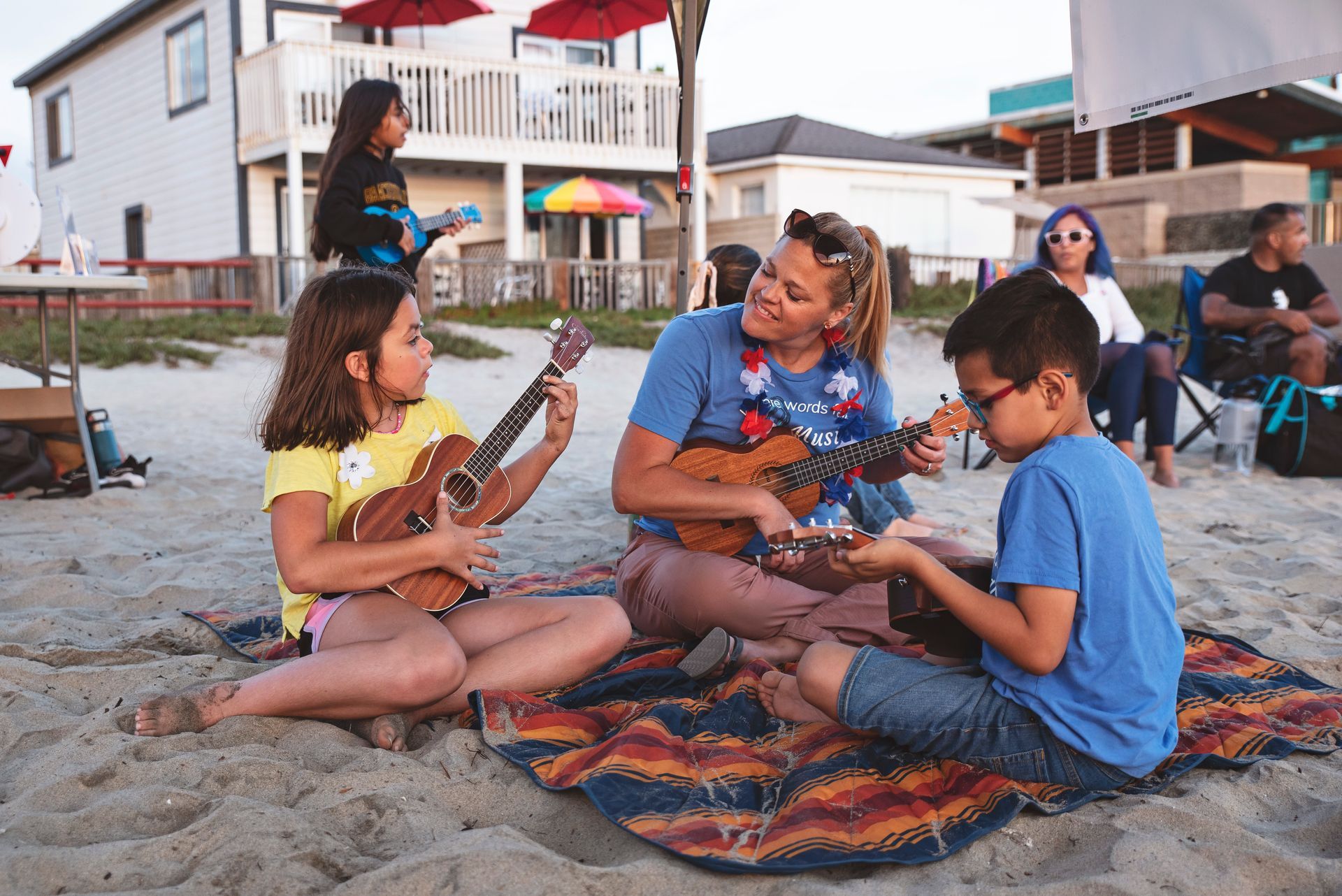 A group of people are sitting on the beach playing ukuleles.