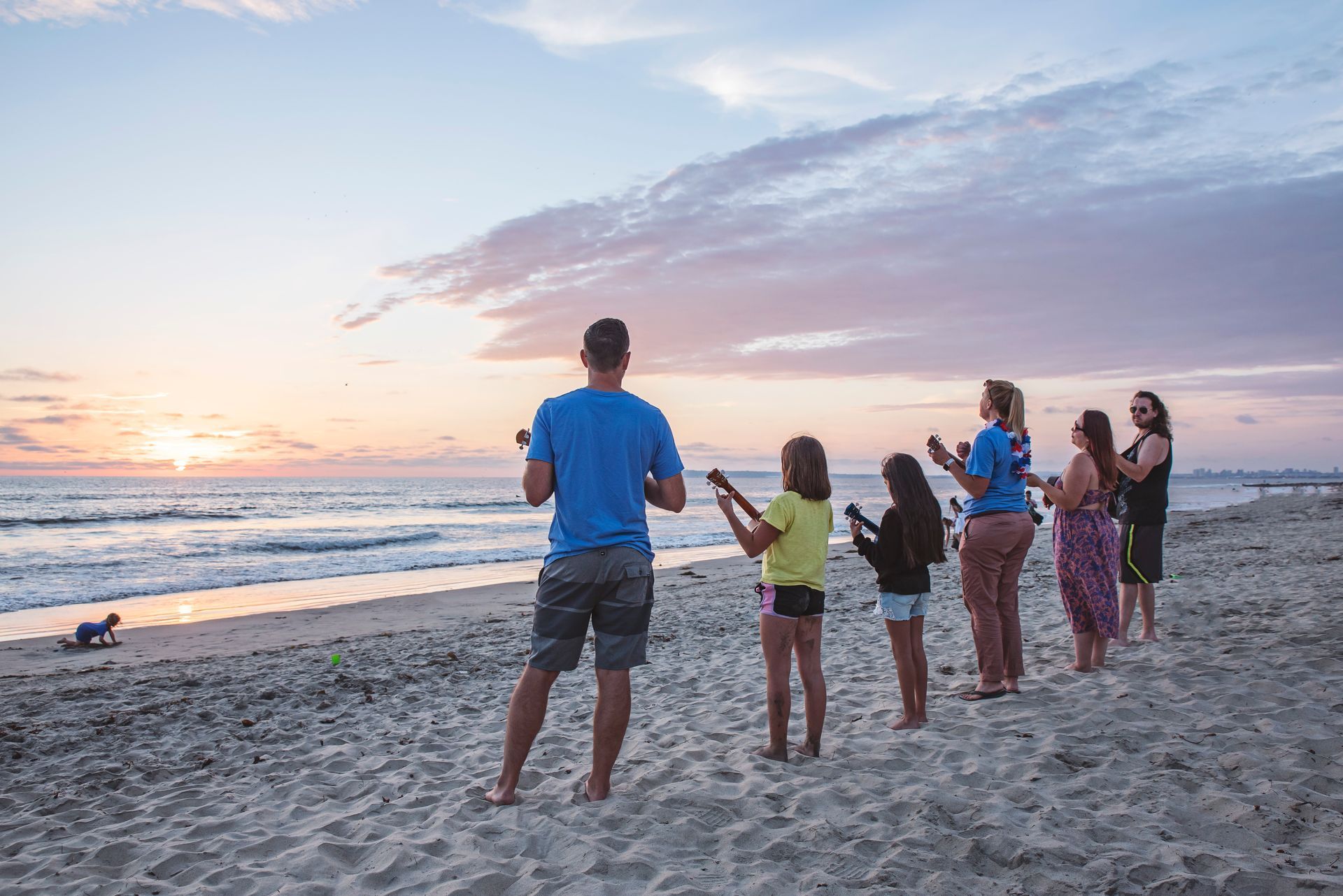 A group of people are standing on a beach watching the sunset.