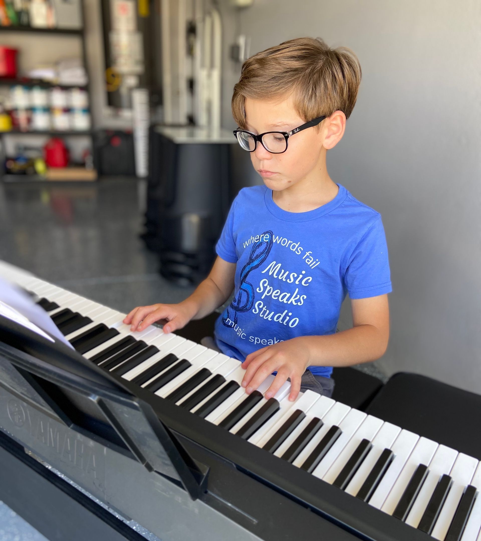 A young boy is playing a piano in a garage.