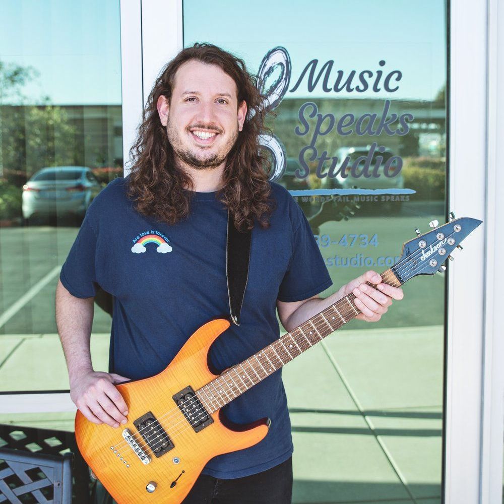 A man holding a guitar in front of a music speaks studio