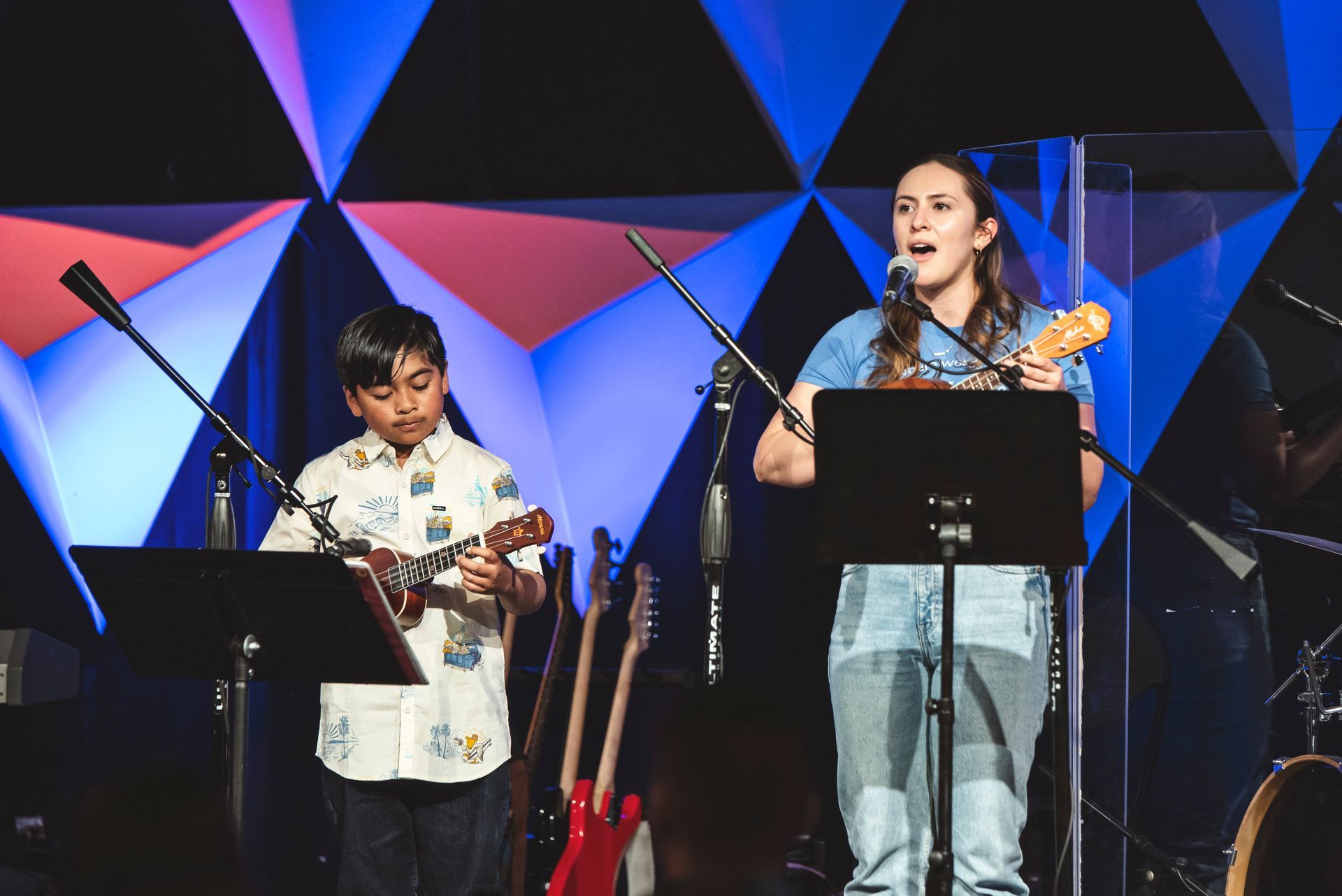 A young boy is playing an acoustic guitar in front of a man.