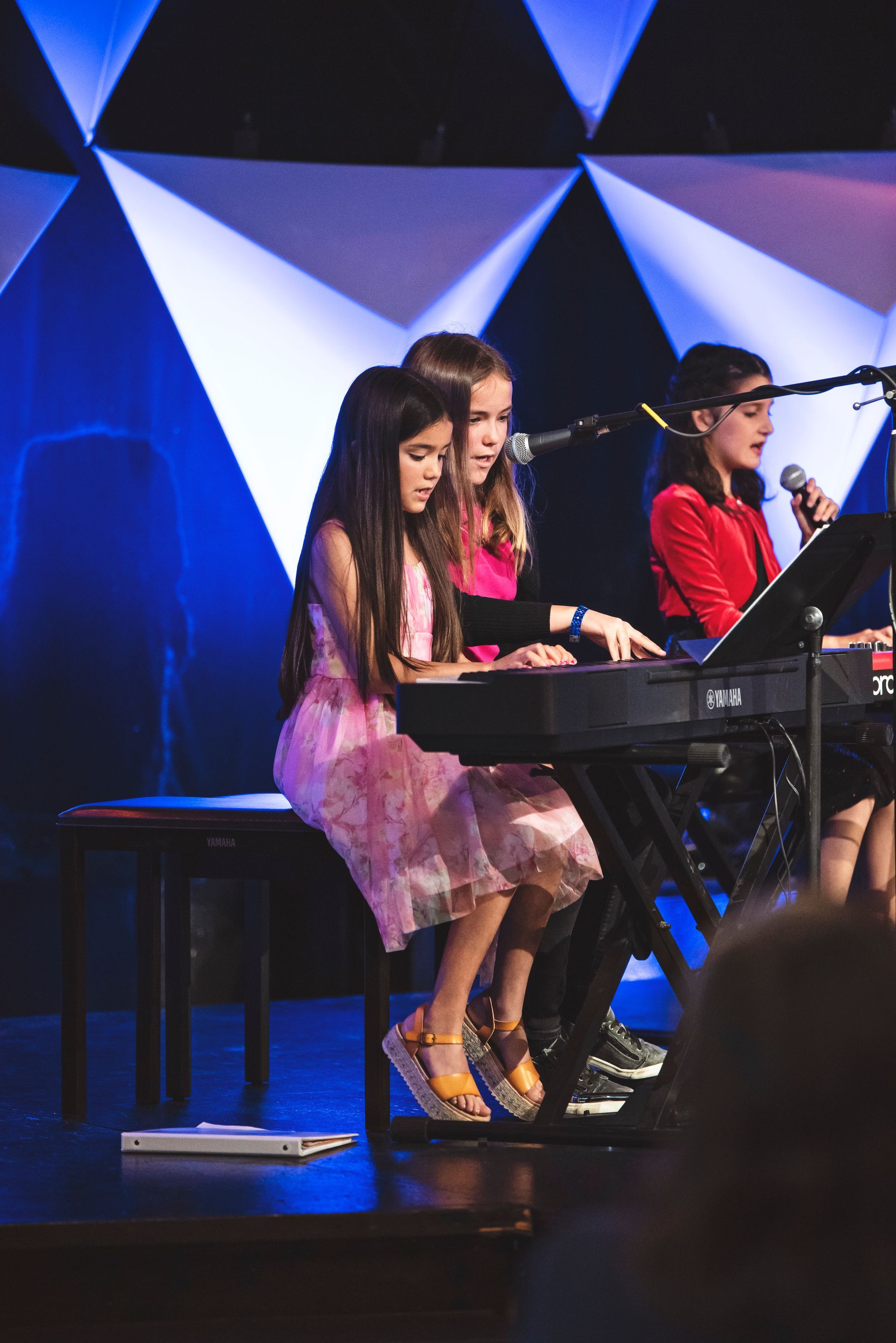 A group of young girls are playing keyboards and singing on a stage.