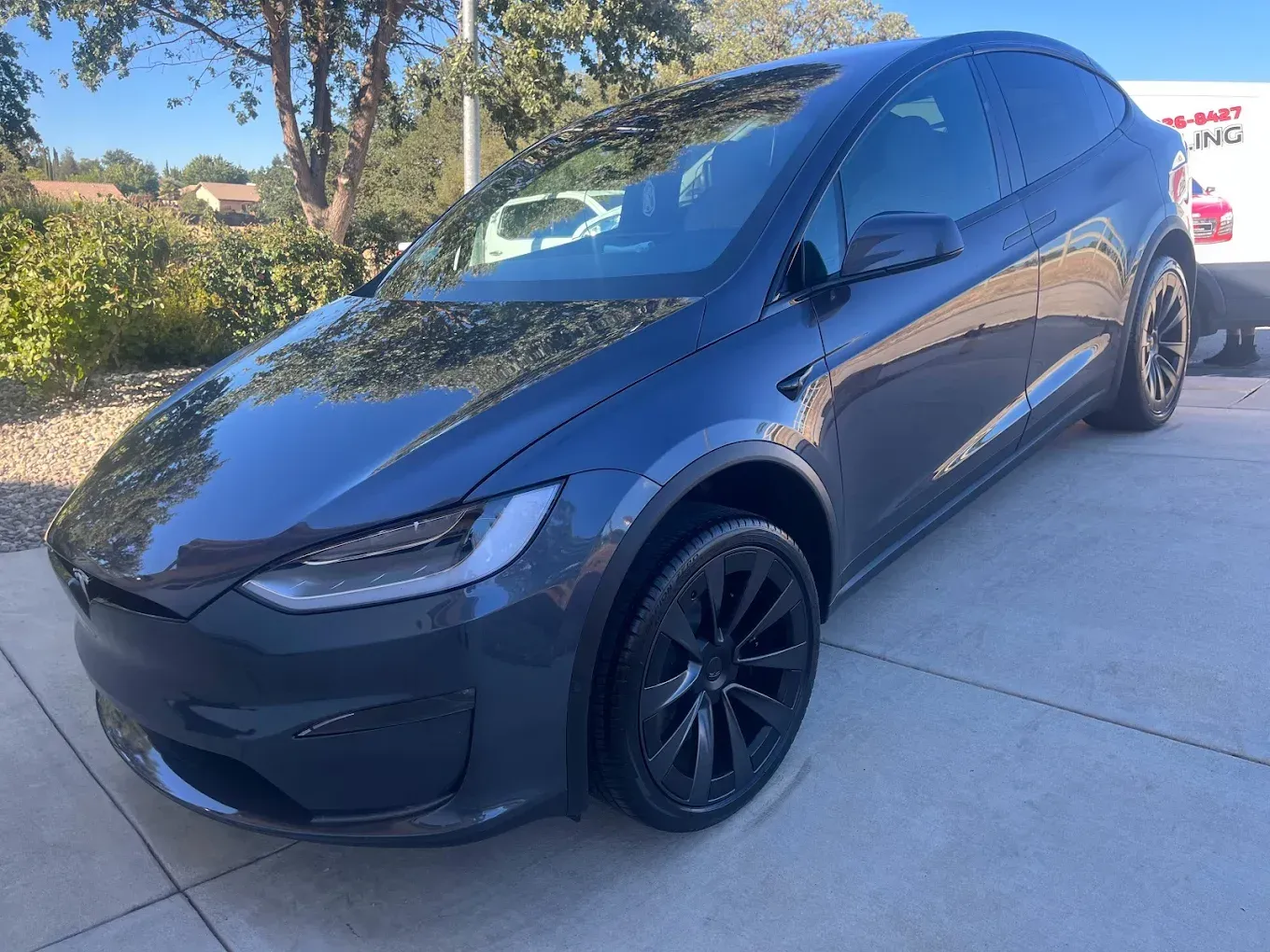 Dark gray Tesla Model X SUV parked on a paved surface, under a bright blue sky.