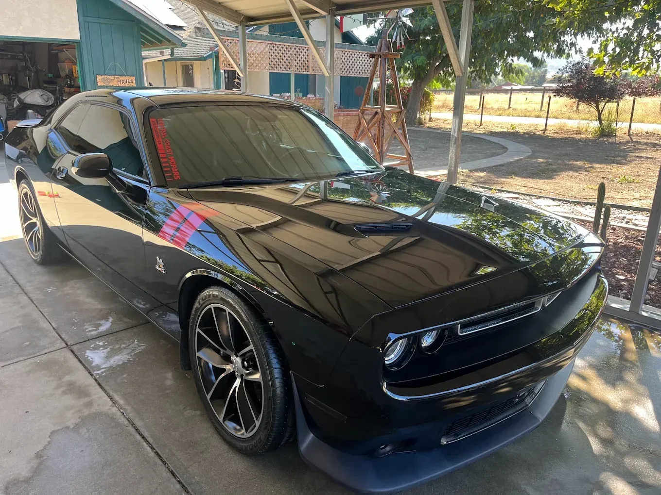Black Dodge Challenger parked under a covered area. Red stripe detail on hood.
