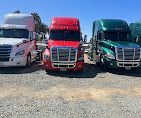 Three semi-trucks parked outdoors, white, red, and green.