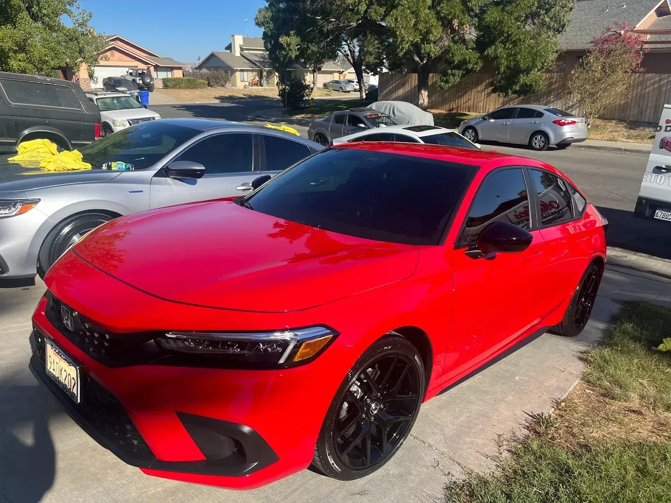 Red Honda Civic parked on a sunny street with other cars. Black rims, tinted windows.