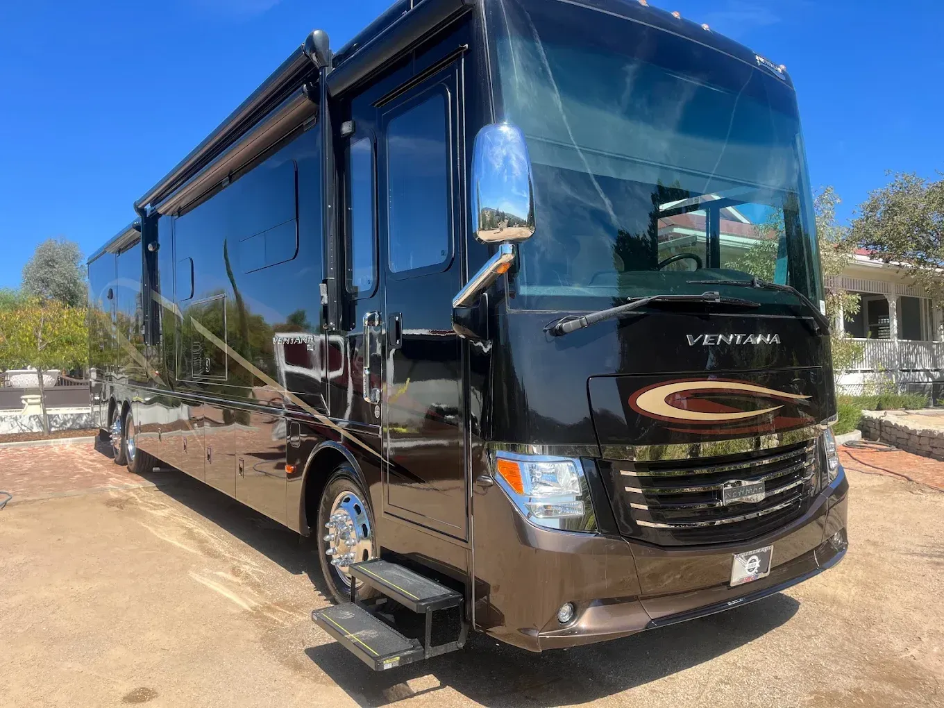 Dark brown luxury RV parked on a brick and concrete surface on a sunny day.