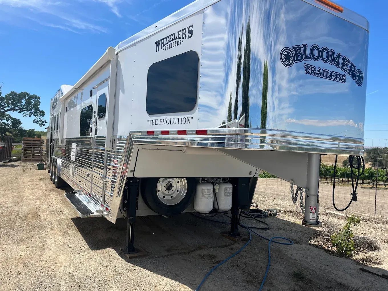 Shiny white and chrome Bloomer horse trailer parked outdoors.