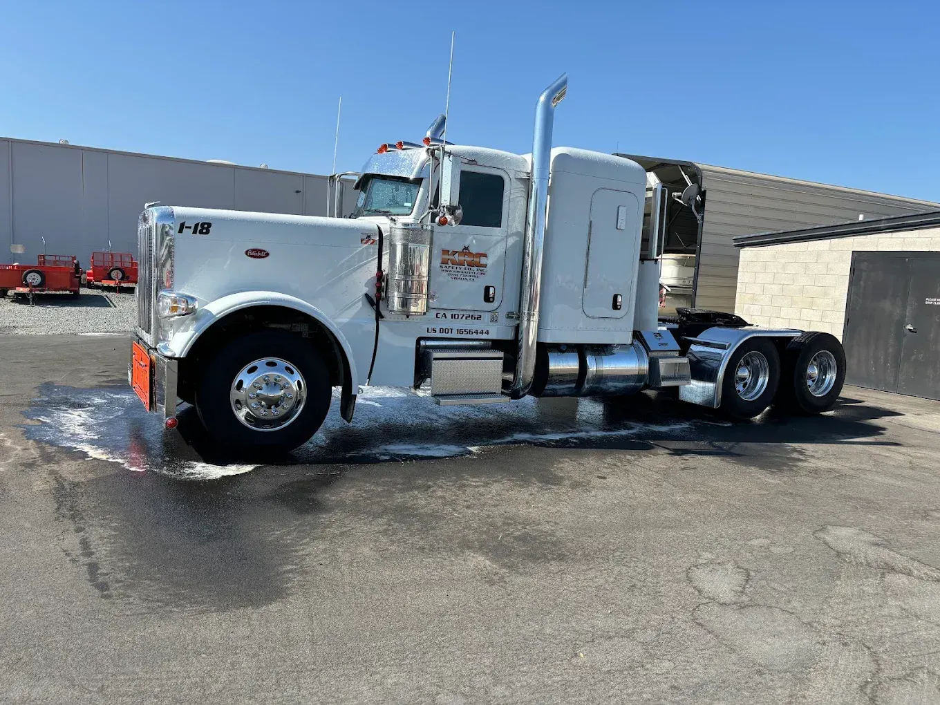 White Peterbilt semi-truck being washed outdoors with a building in the background.