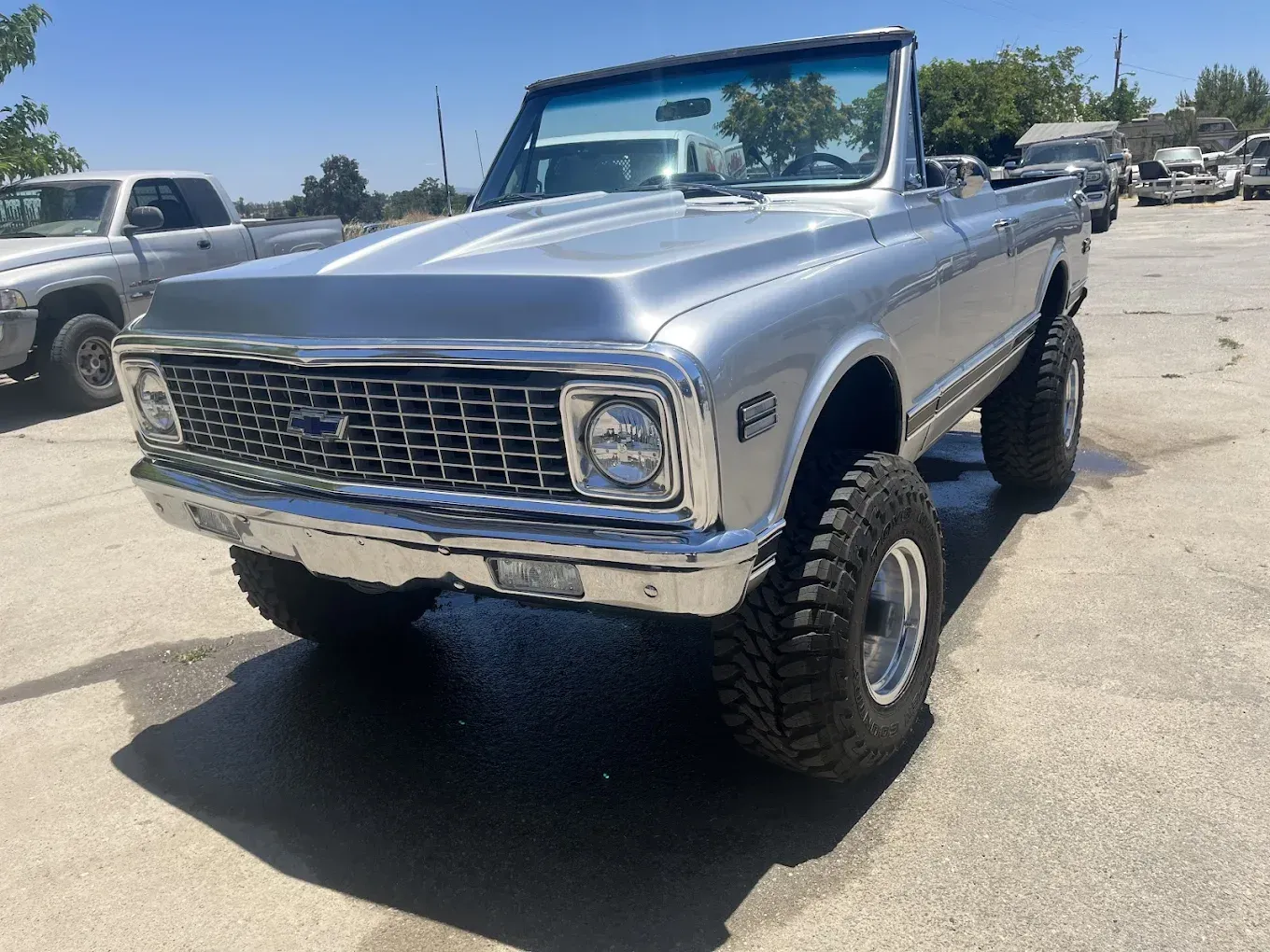 Silver vintage Chevrolet Blazer convertible, lifted with large tires, parked outdoors.