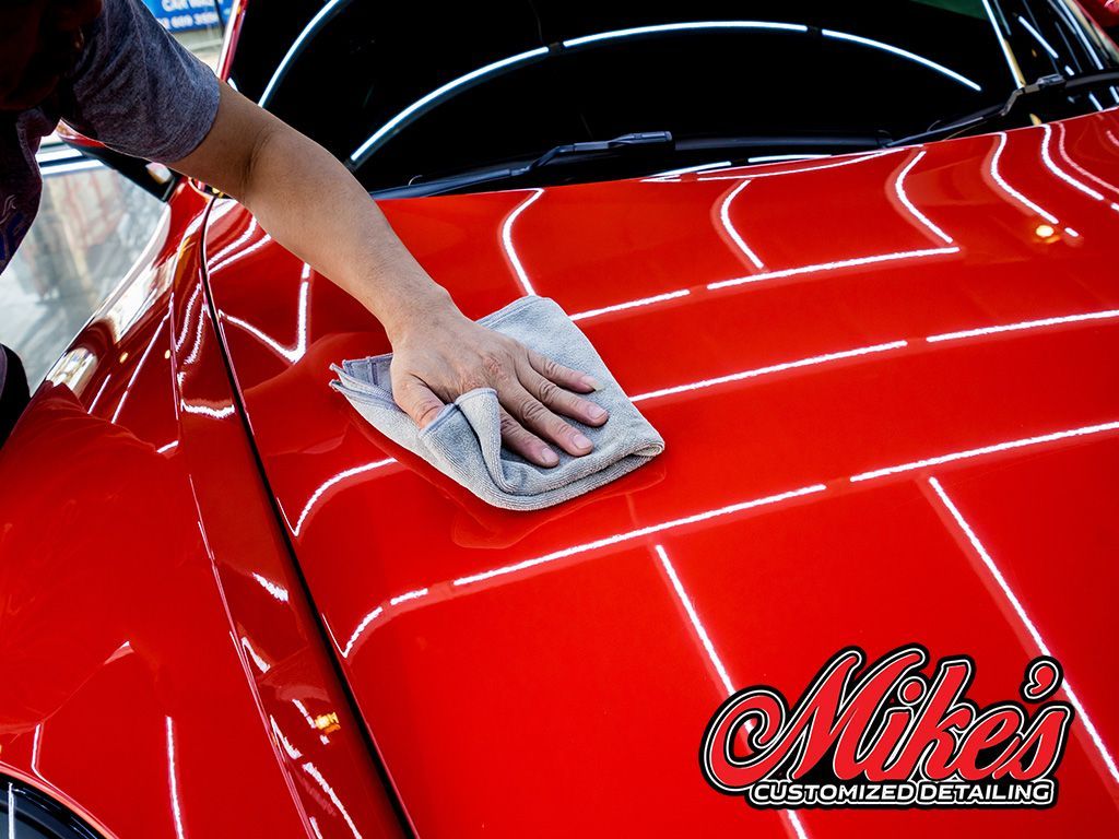 A person polishing a red car with a microfiber cloth.