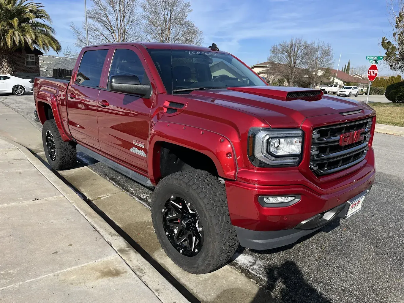Red GMC Sierra truck with black wheels parked on a street curb.