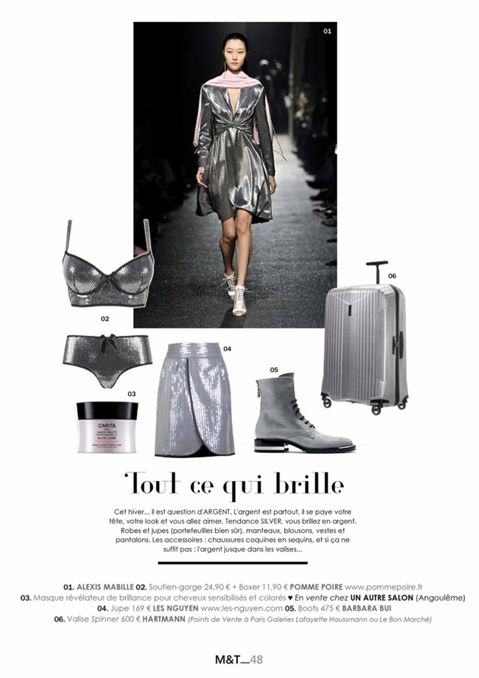 Une femme marche sur un podium vêtue d'une robe argentée et d'une valise.