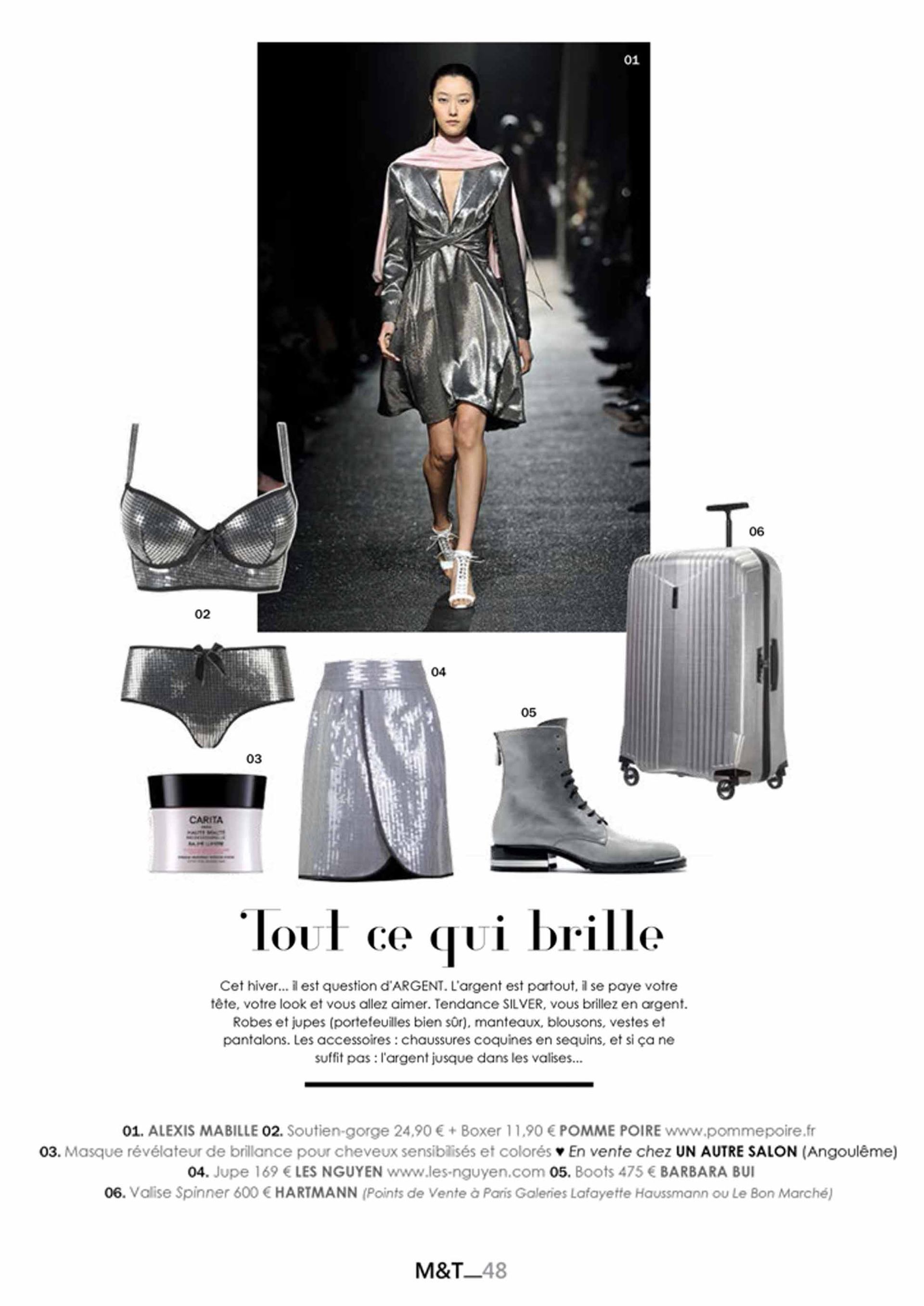 Une femme marche sur un podium vêtue d'une robe argentée et d'une valise.