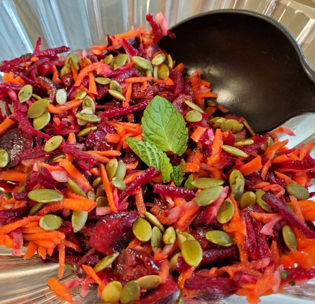 A salad with carrots beets and pumpkin seeds in a bowl with a spoon