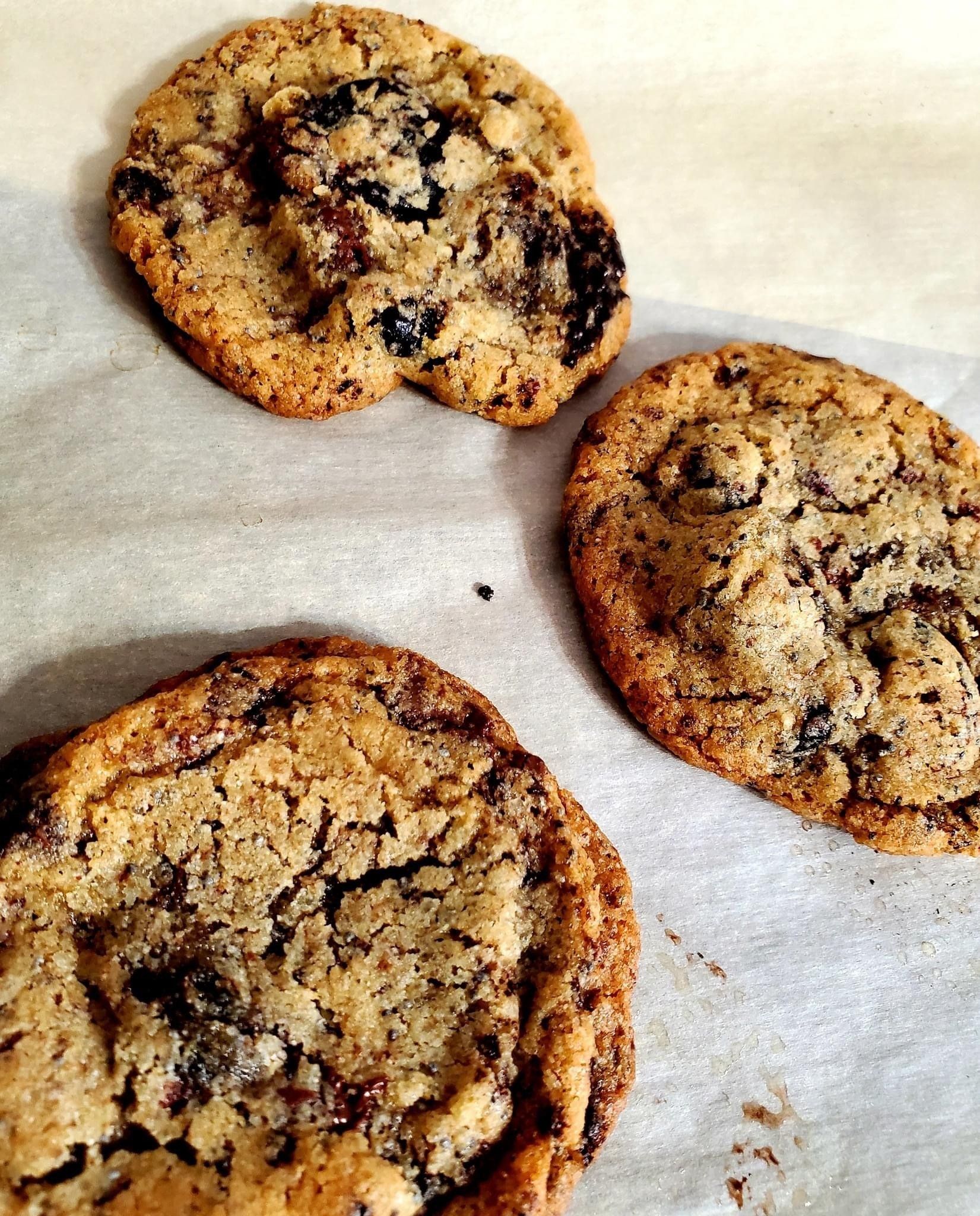 Three chocolate chip cookies are sitting on a piece of wax paper