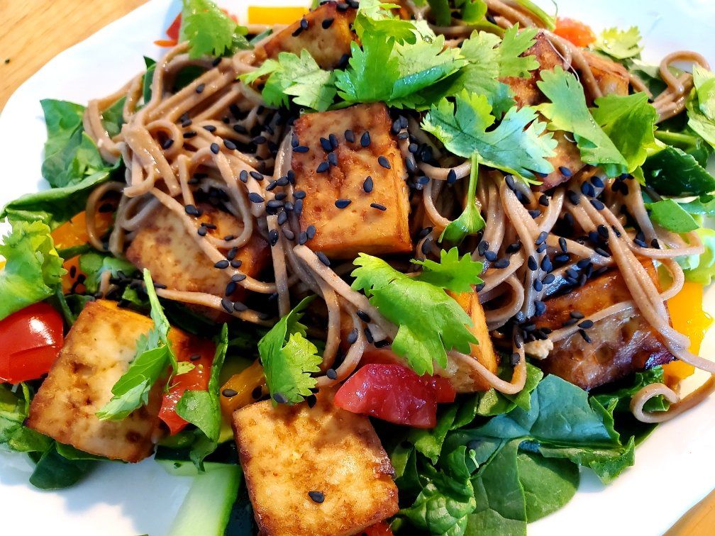 A white plate topped with noodles tofu and vegetables