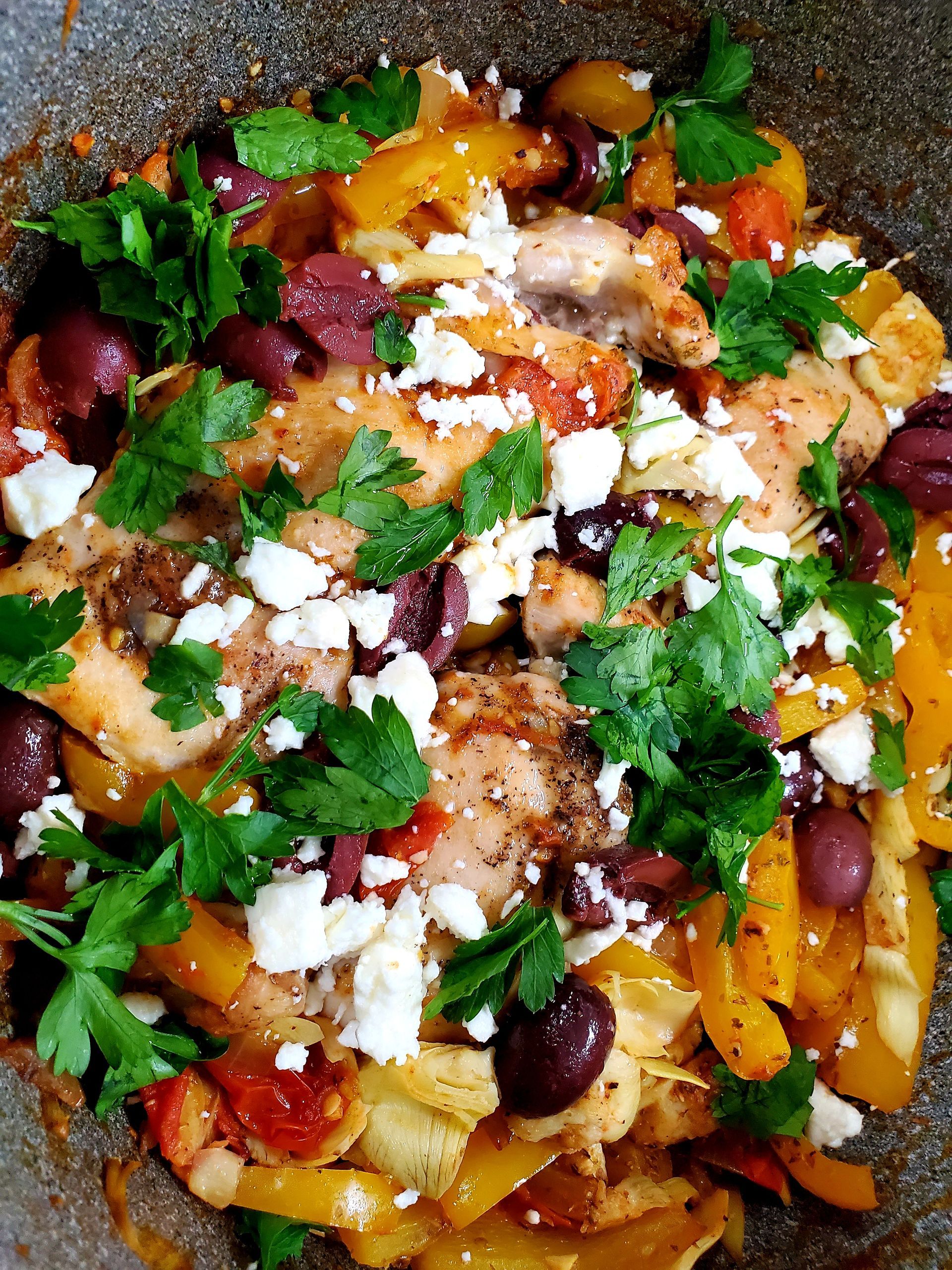 A close up of a plate of food with chicken , olives , cheese and parsley.