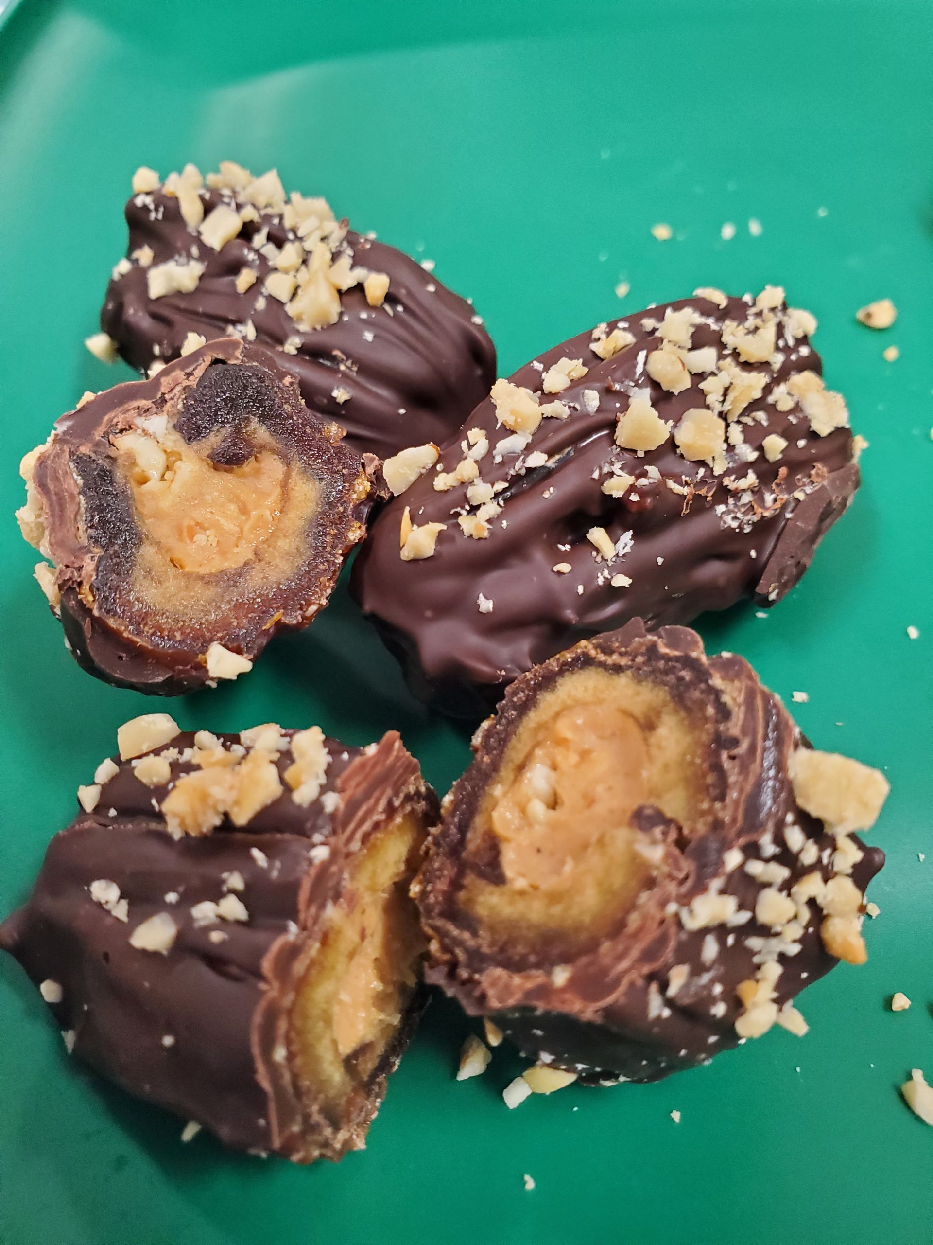 A close up of chocolate covered dates with nuts on a green plate
