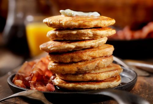 A stack of pancakes with butter and bacon on a plate.