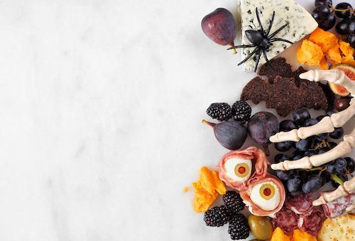 A halloween appetizer board with a skeleton hand , spiders , grapes , olives and cheese.