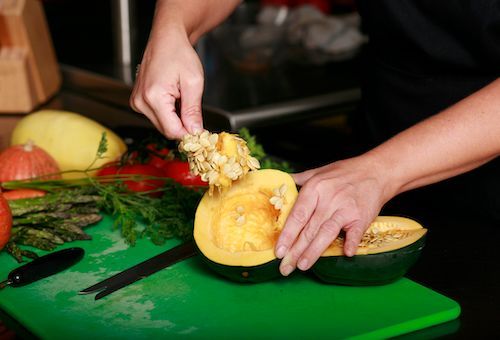A person is cutting a squash on a green cutting board.