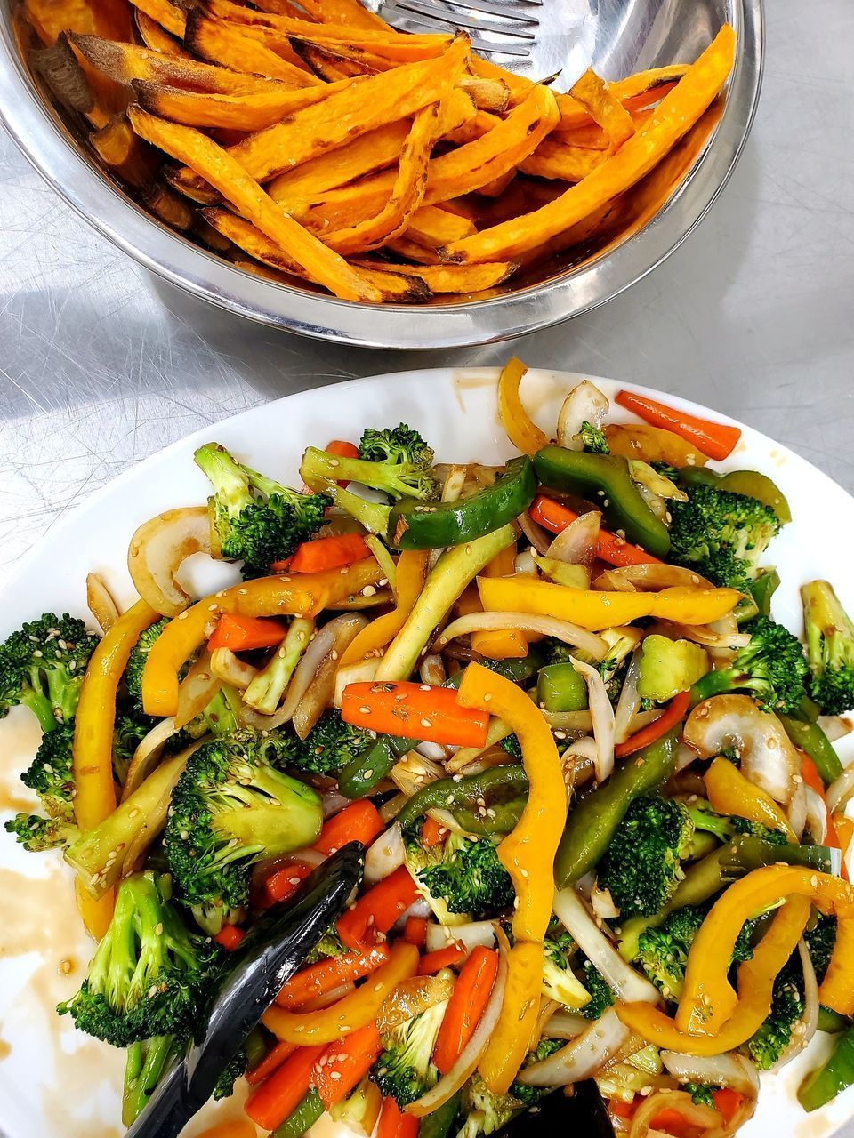 A plate of vegetables next to a bowl of sweet potato fries.