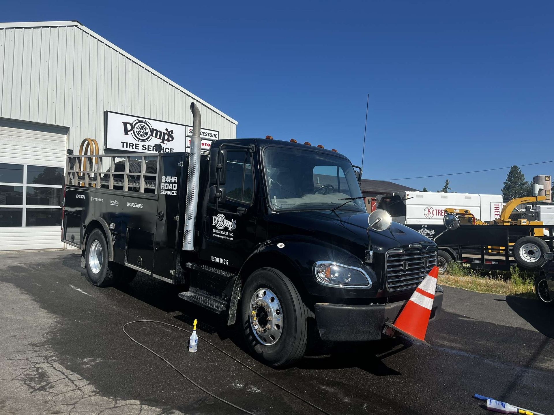 Black work truck parked outside a building on a sunny day. The truck has a tall exhaust pipe and a traffic cone on the front.