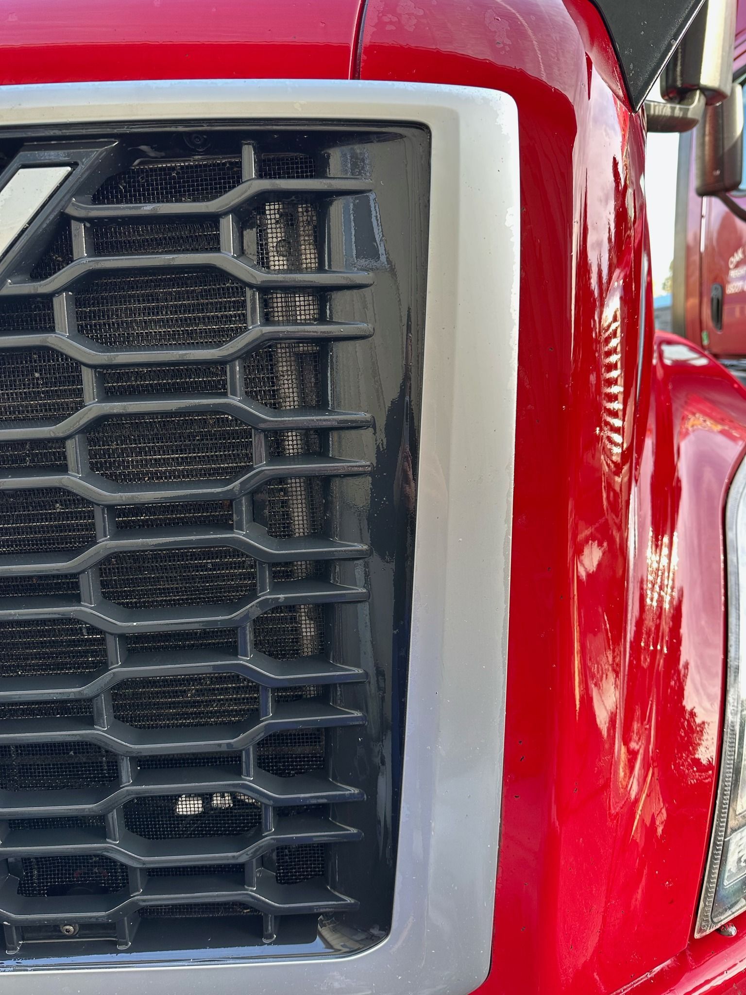 Close-up of a red semi-truck grill with a black honeycomb pattern and a silver border.