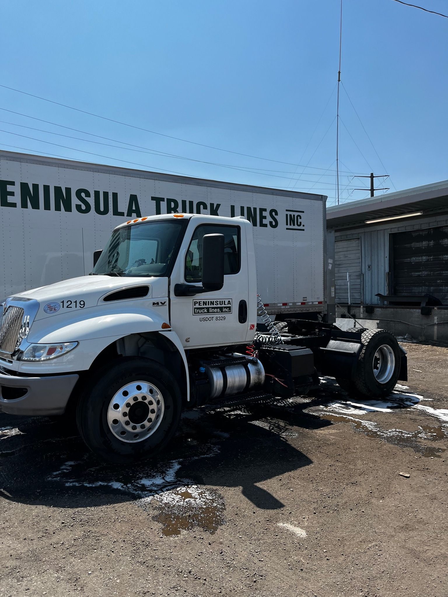 White semi-truck parked in front of a loading dock. The truck has the Peninsula Truck Lines logo.
