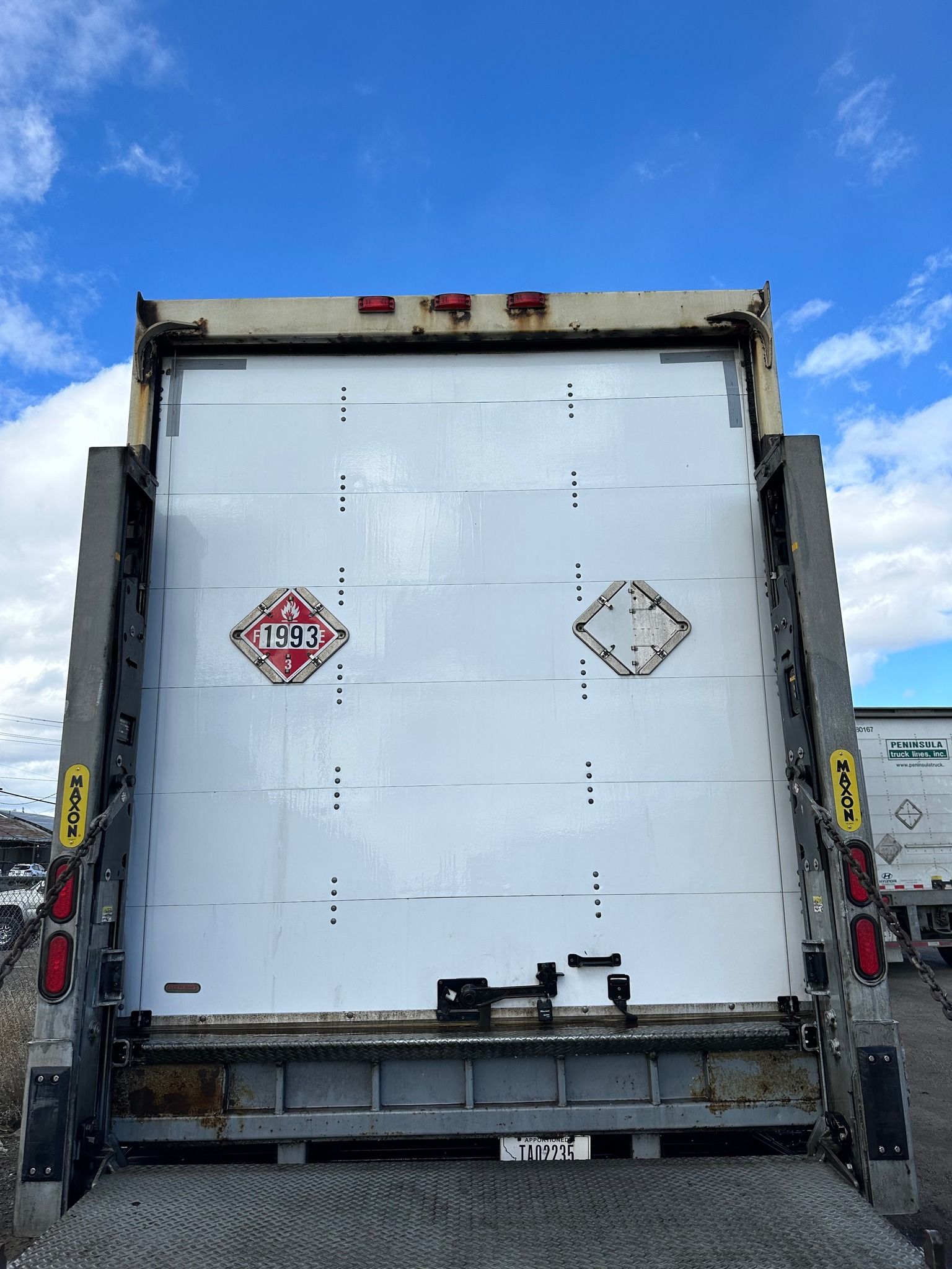 Back of a white delivery truck with hazmat placards against a blue sky.