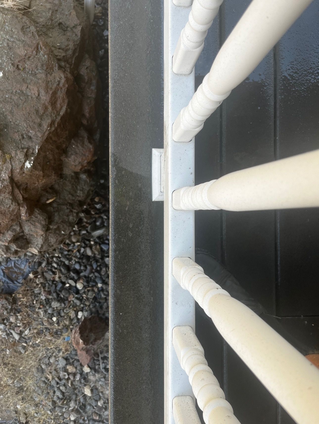 White railing with spindles on a dark surface next to a rock and stone area.