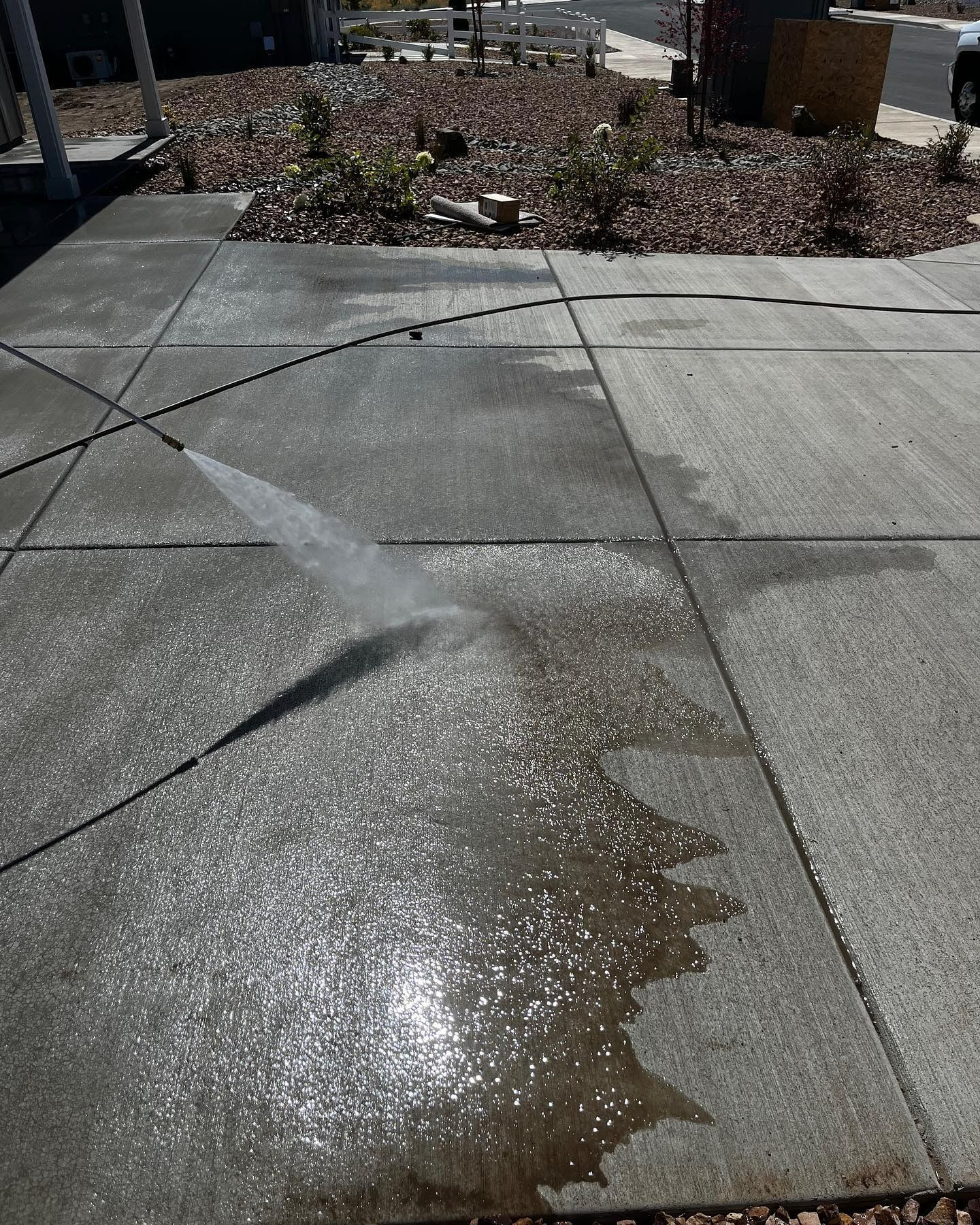 A person sprays a sidewalk with water, leaving a wet, shiny patch on the concrete.