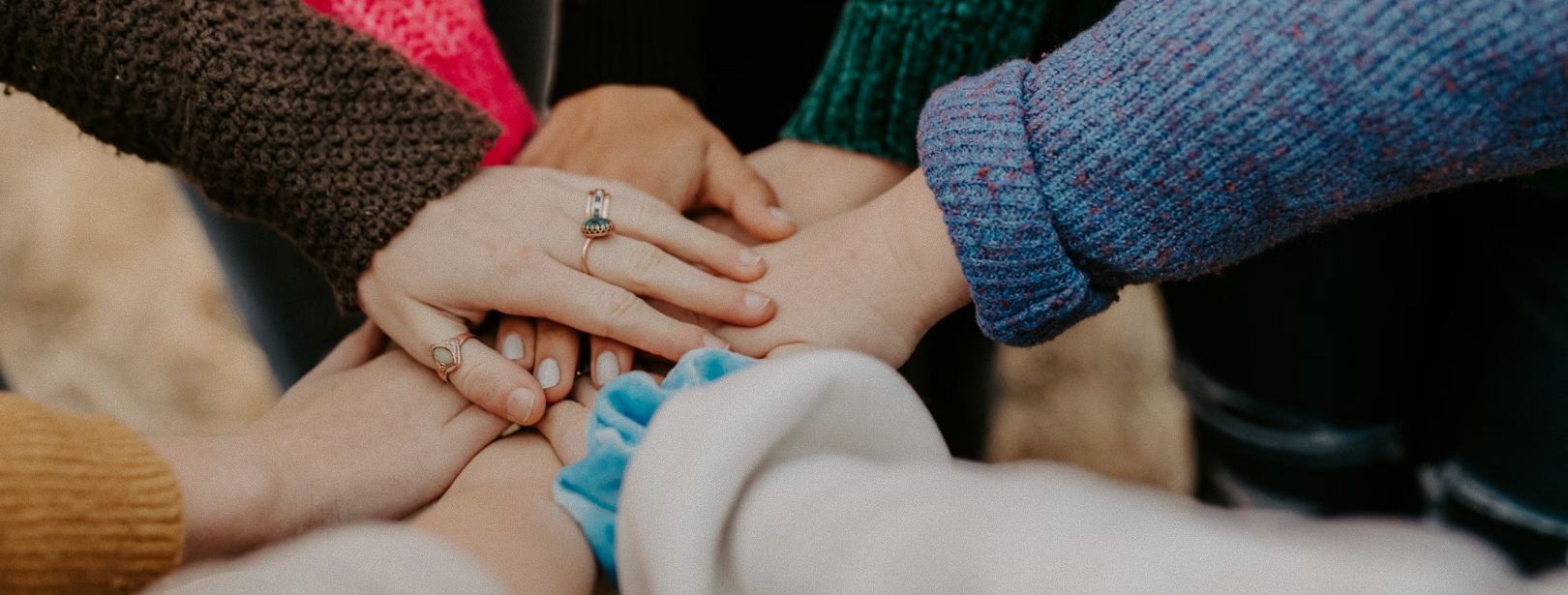 Two people holding hands, offering comfort. Blurred green background.