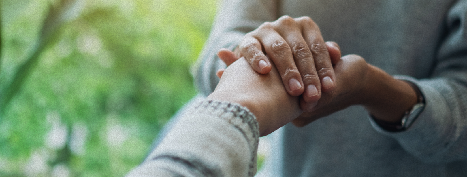Two people holding hands, offering comfort. Blurred green background.
