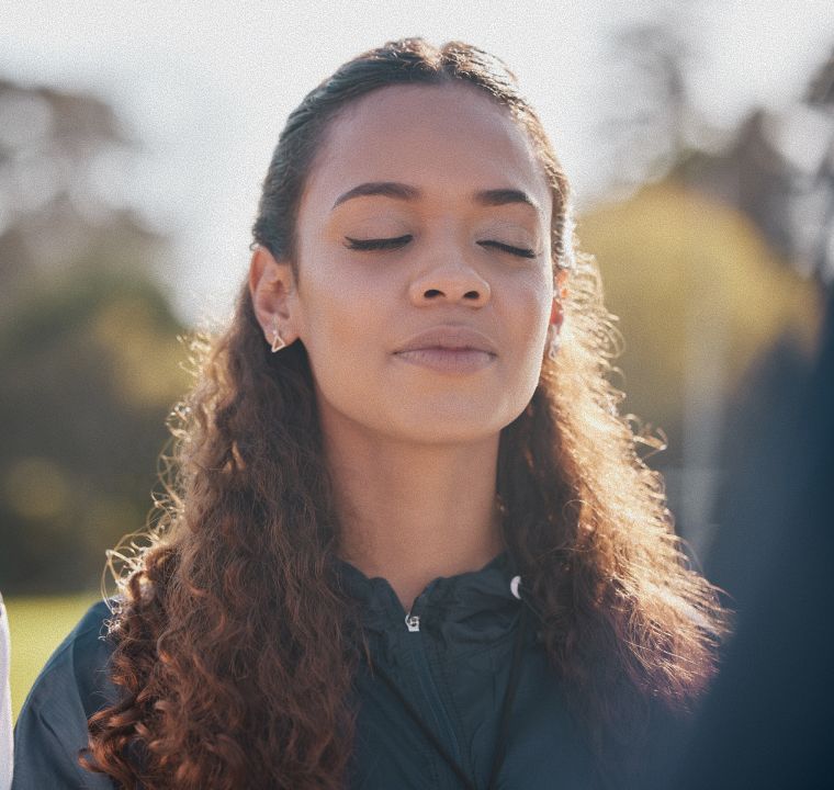 Young person looking up, outdoors. Soft sunlight, trees in background.