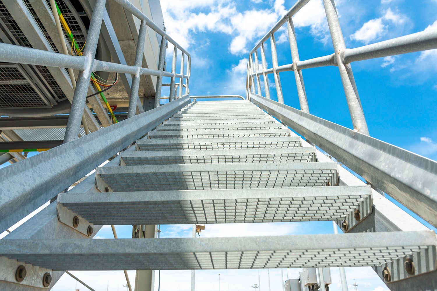A metal staircase with a railing and a blue sky in the background.