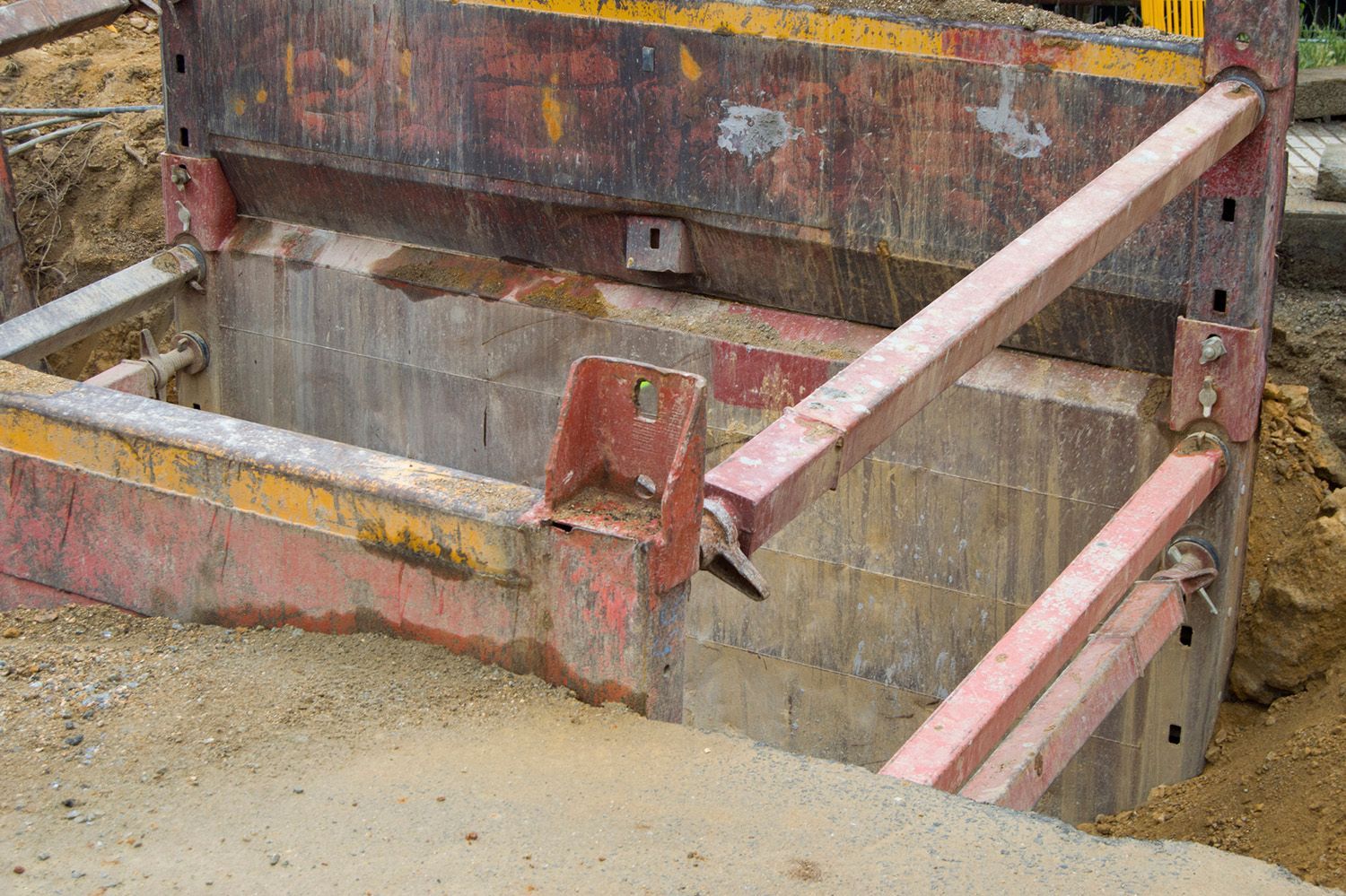 A large metal structure is sitting in the dirt next to a concrete wall.