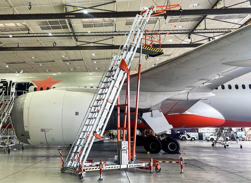 A large metal structure is sitting in the dirt next to a concrete wall.