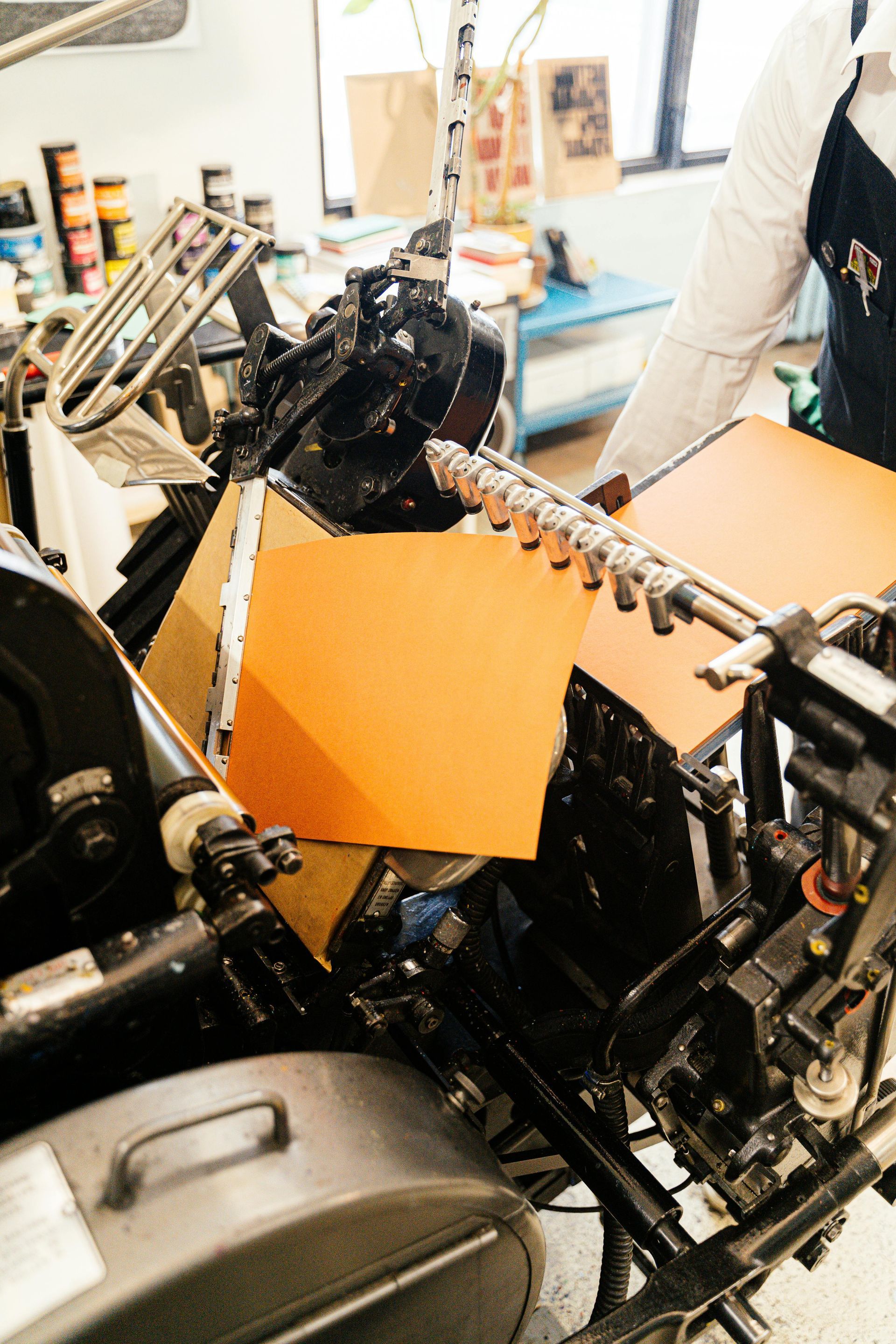 Person operating a vintage printing press with orange paper.